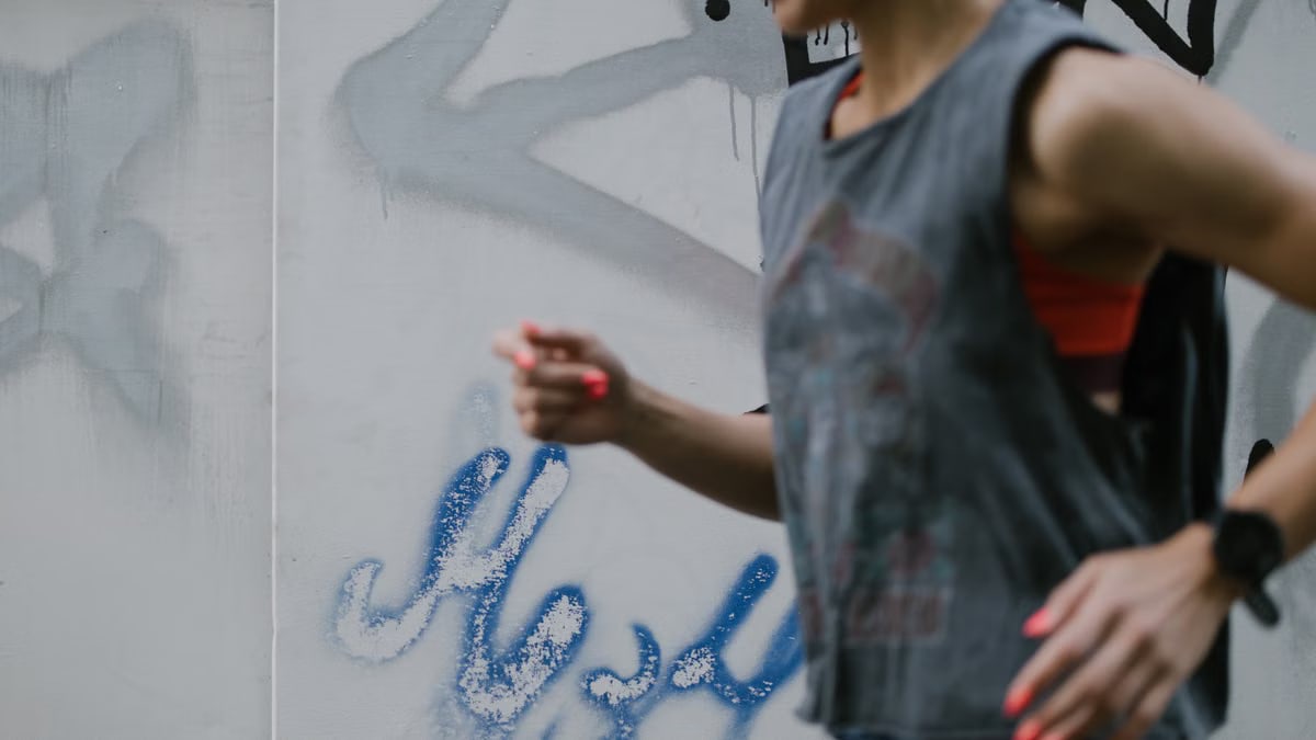 Woman in motion running alongside a graffiti-covered wall, embodying urban fitness.